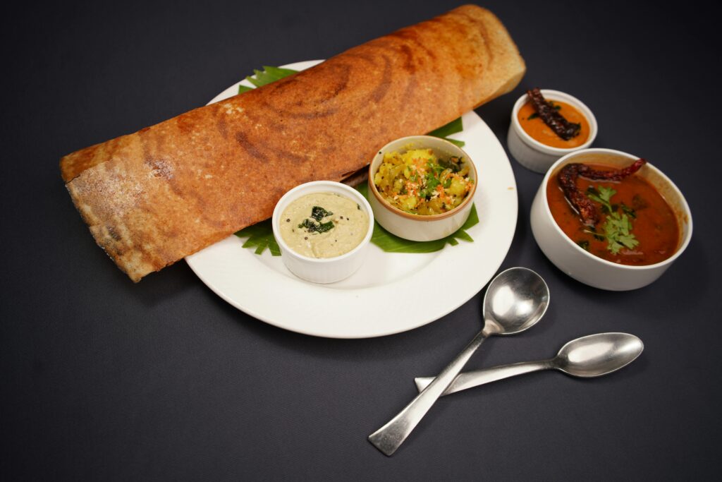 Crispy dosa served with coconut chutney, vegetable curry, and sambar on a black background.