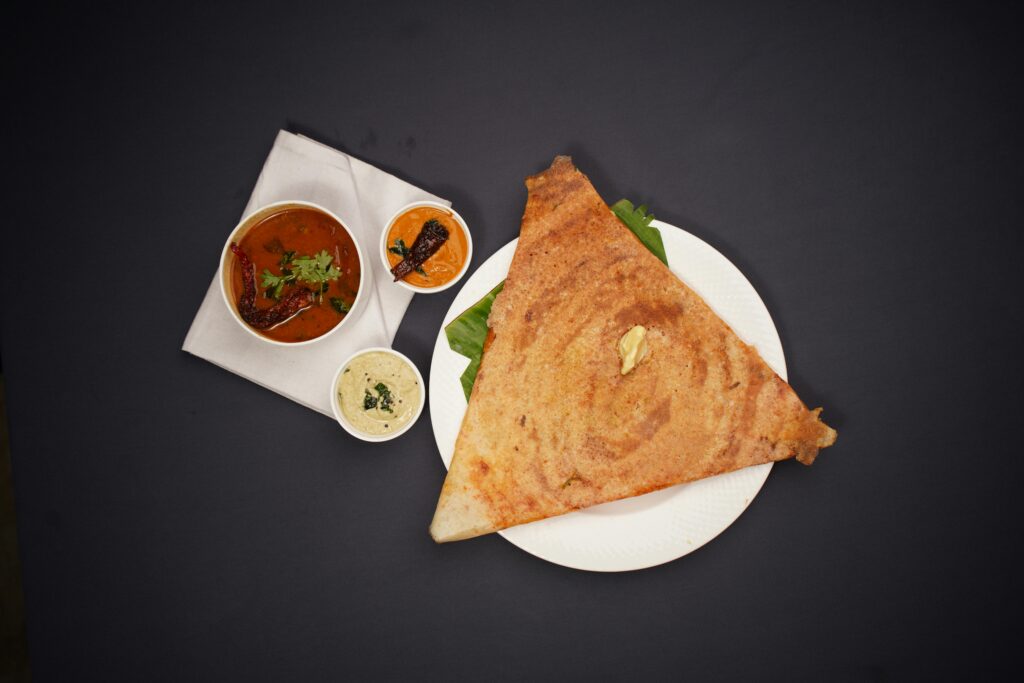 Top view of masala dosa with chutneys and sambar on a black background. Perfect for food photography.