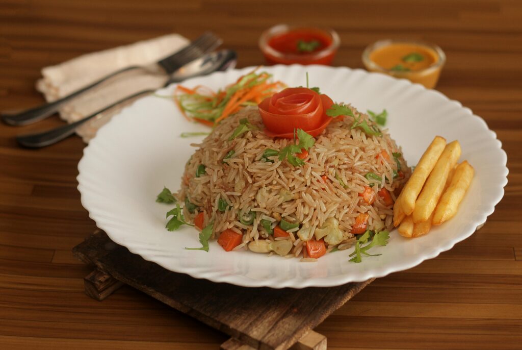 Tasty vegetable fried rice with a tomato rose and fries on a wooden background.