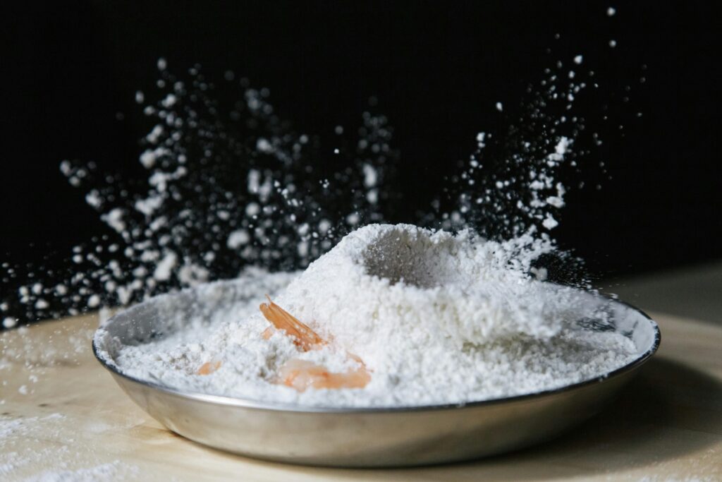 Dramatic capture of flour splash with shrimp in a metallic bowl on dark background.